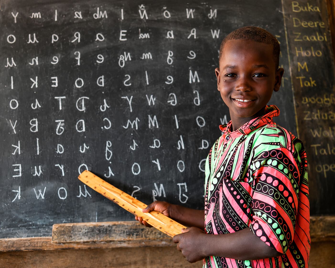 Jeune garçon nigérien devant un tableau noir d'apprentissage, vêtement traditionnel coloré, symbole de l'éducation que TAIMAKAB FOR HUMANITY soutient